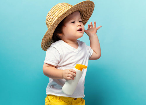 Kid in hat holding sunscreen bottle while Mom is talking to him